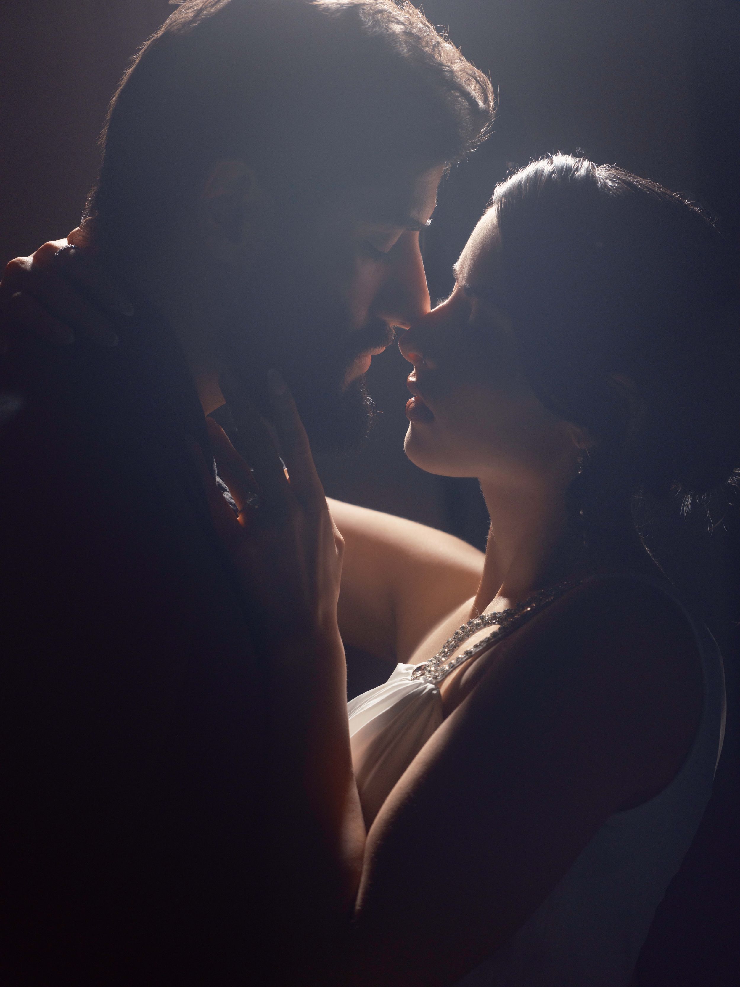 A dramatic silhouette of a couple in an intimate moment, illuminated by rim lighting against a dark background.