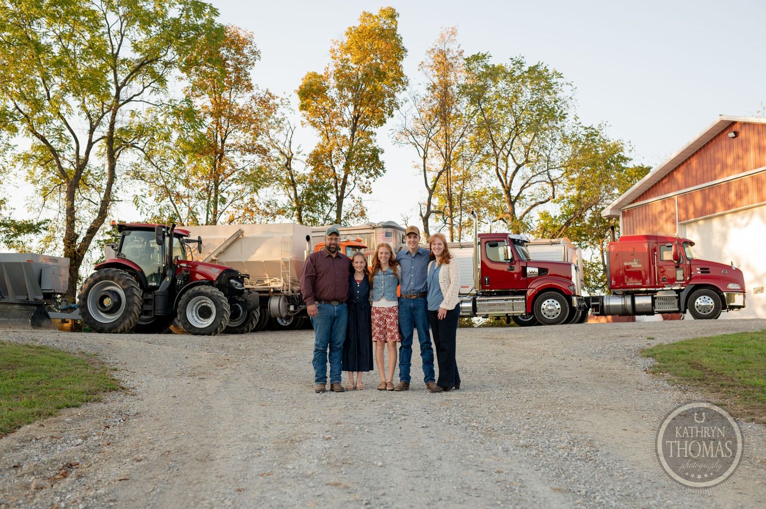 Family group photo with farming equipment and red barn in background.