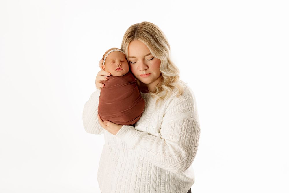 Tender moment between mother and swaddled baby against white studio background.