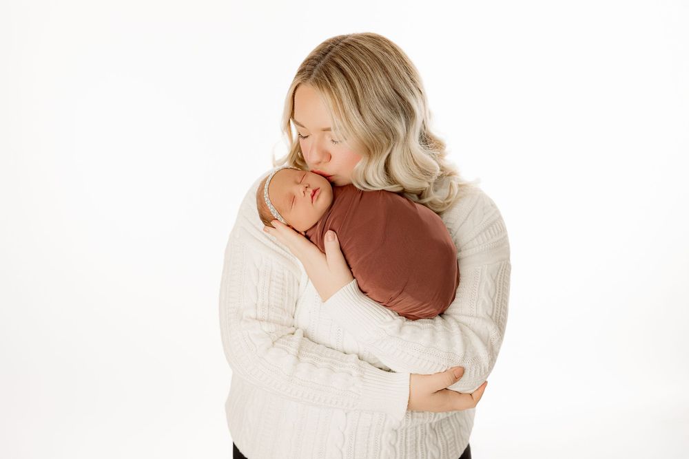Intimate portrait of mother embracing newborn wrapped in brown fabric.