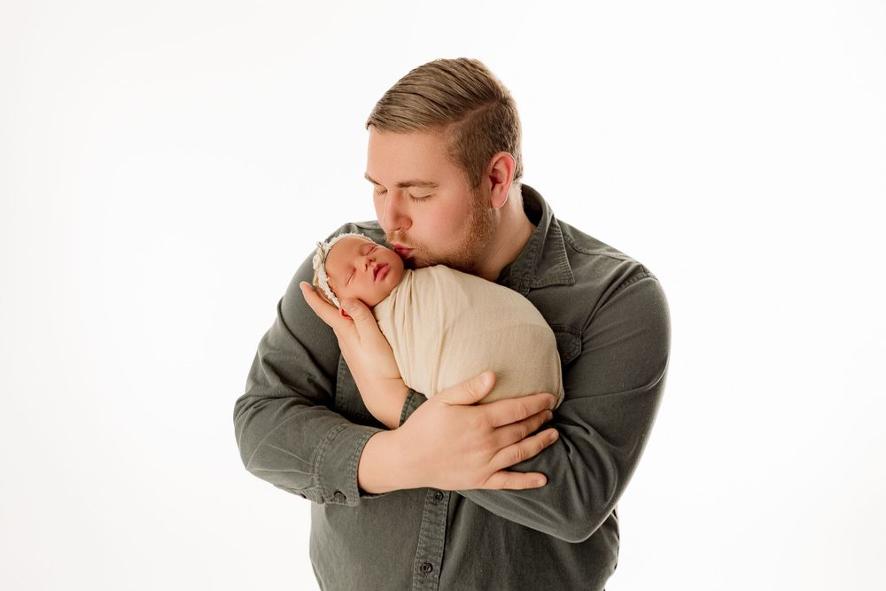 Intimate moment between parent and newborn against white studio background.