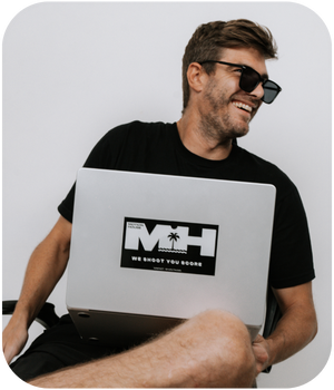 Person in sunglasses working on laptop with MH logo while wearing black t-shirt.