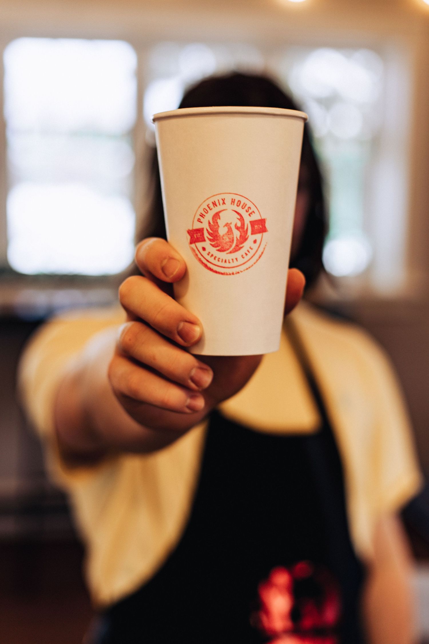 Hand holding white disposable coffee cup with red logo branding.