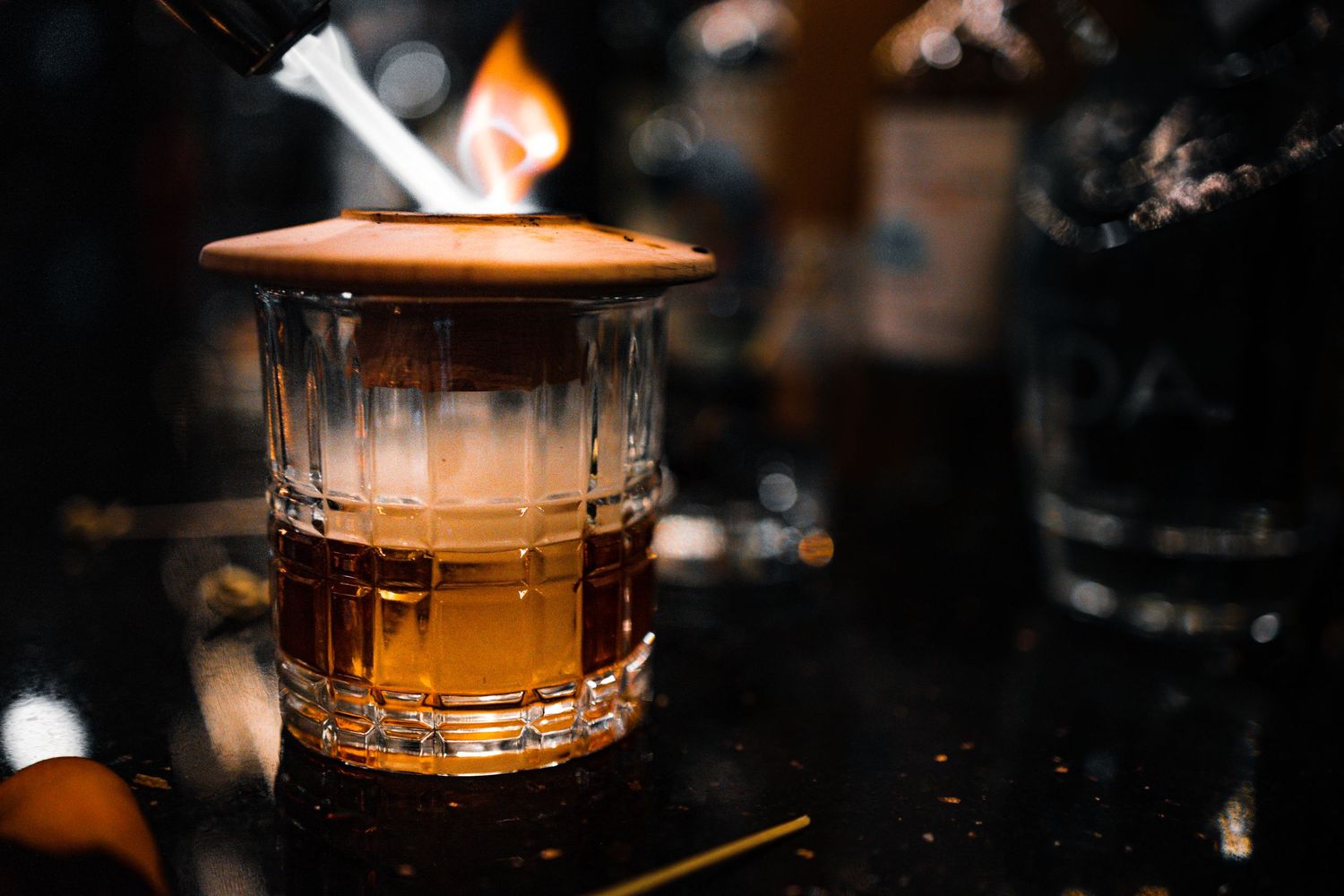 Illuminated glass of amber liquid in moody bar setting.