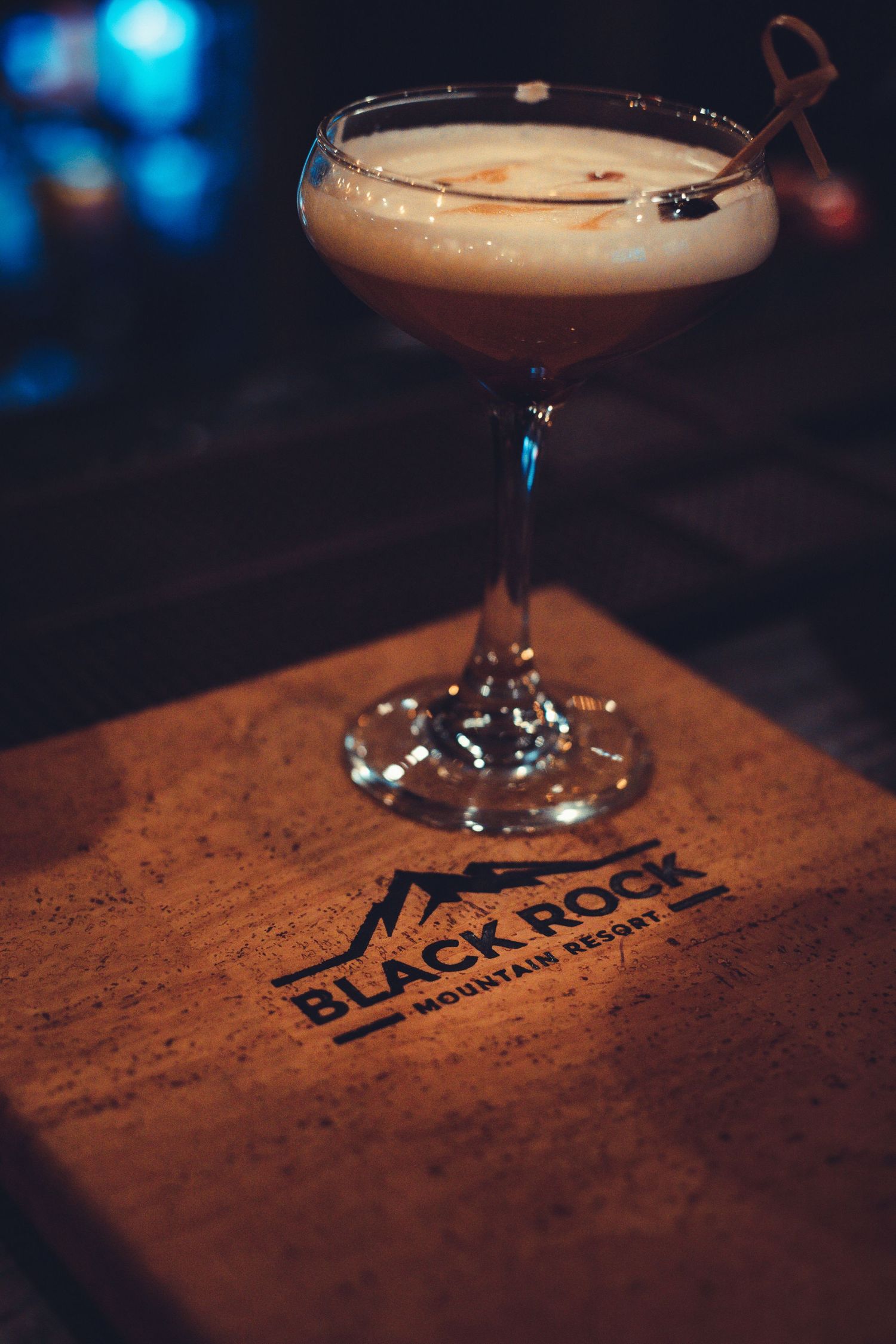 Elegant cocktail in coupe glass on wooden surface with Black Rock branding.