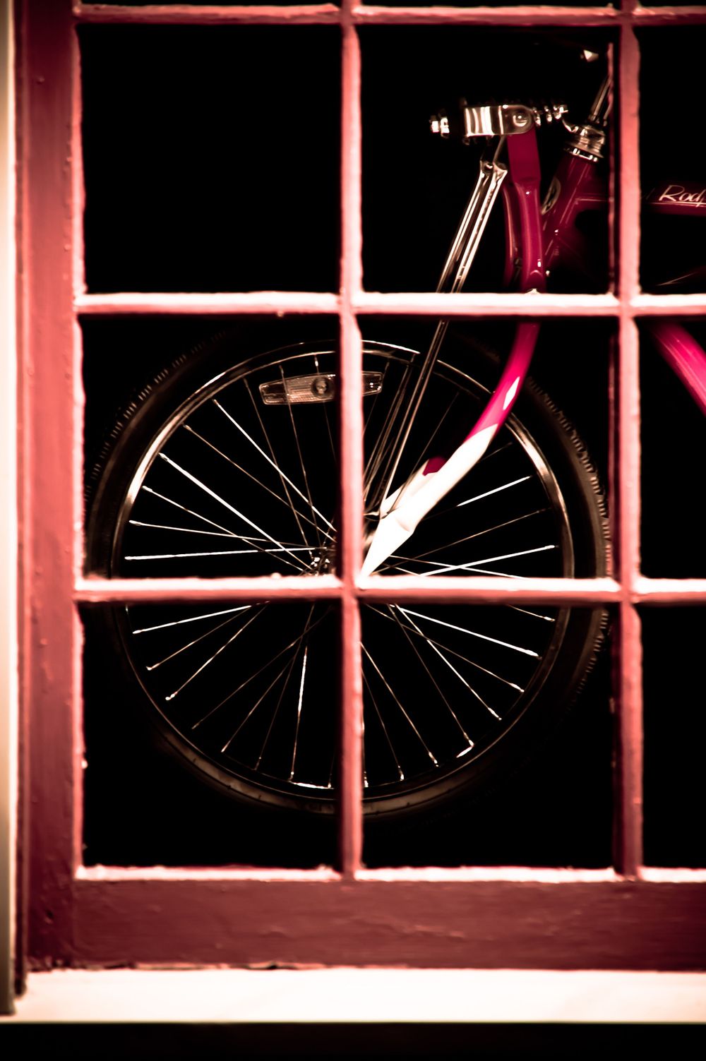 Red bicycle framed by a red, small pane, window