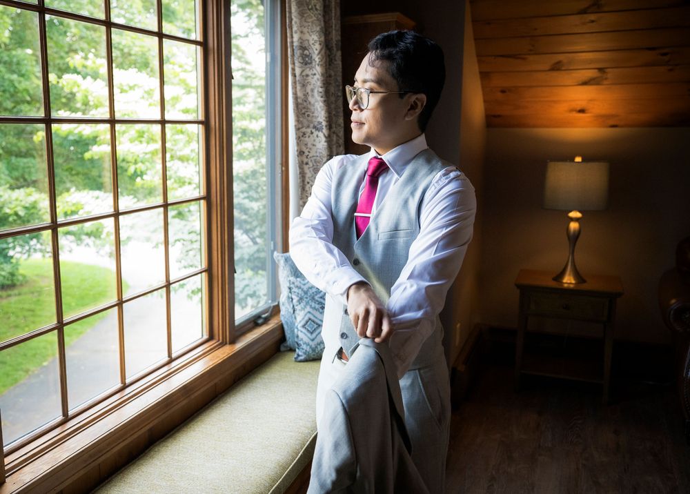 Person in light grey suit with pink tie gazes thoughtfully out a window.