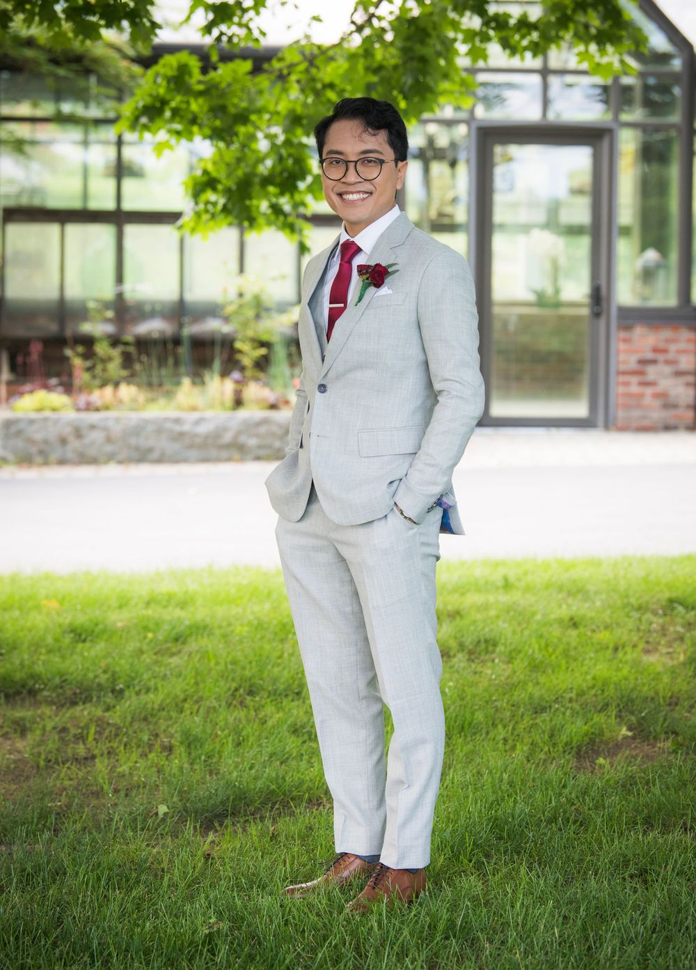 Figure in light gray suit poses gracefully on manicured grass lawn near modern building.