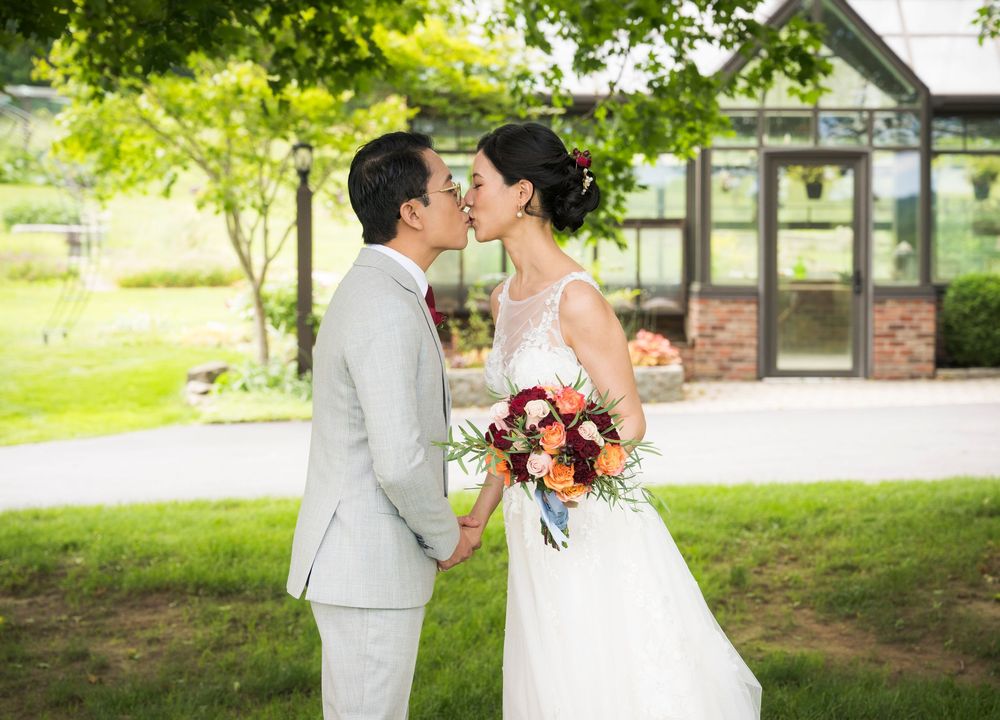 A romantic wedding couple shares a kiss in front of a greenhouse on a sunny day.
