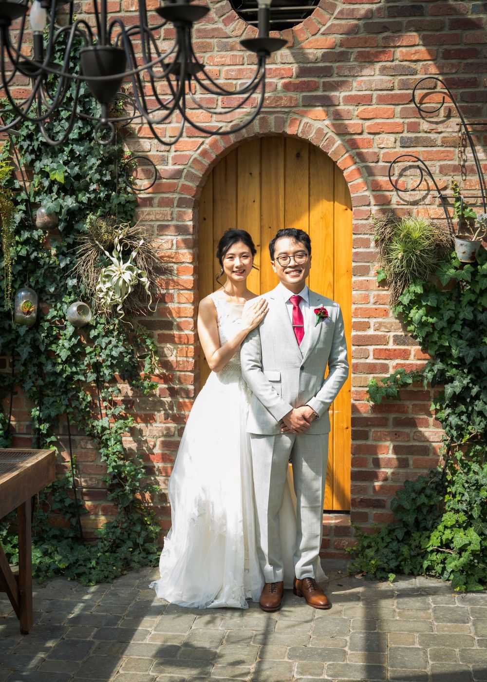 A romantic wedding portrait in front of a brick wall with yellow door and climbing ivy.