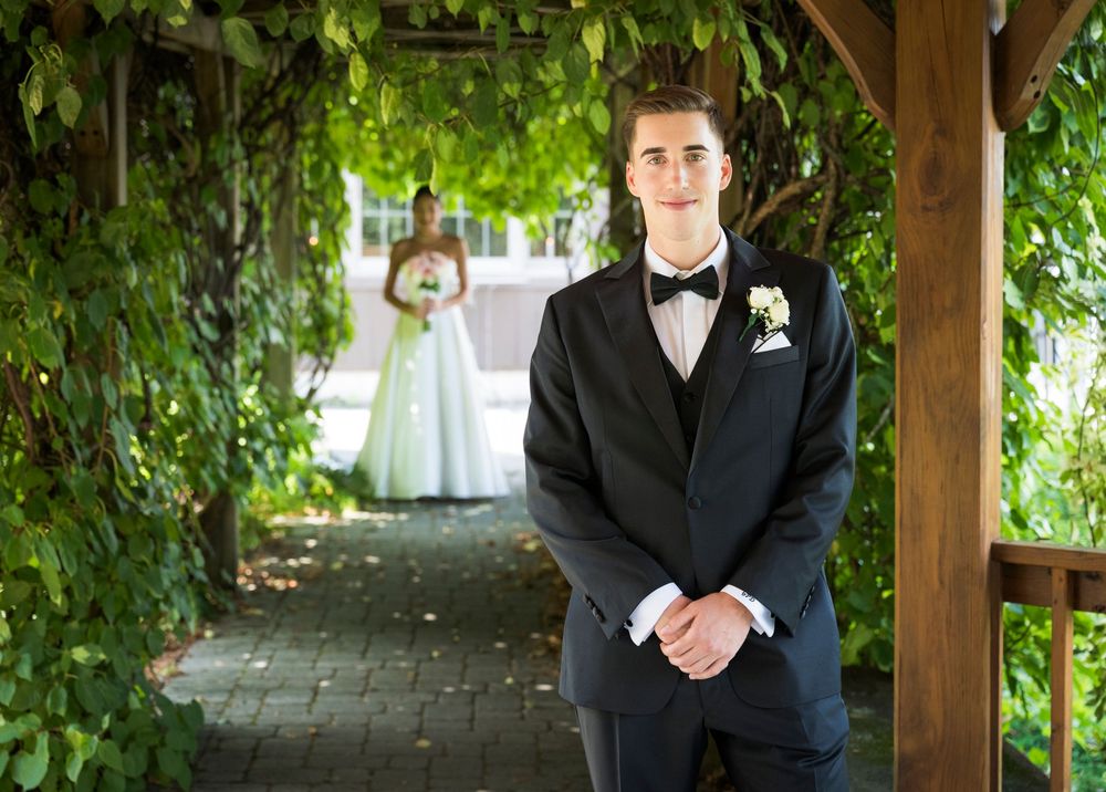 Outdoor wedding venue with green vine-covered wooden pergola and stone pathway.