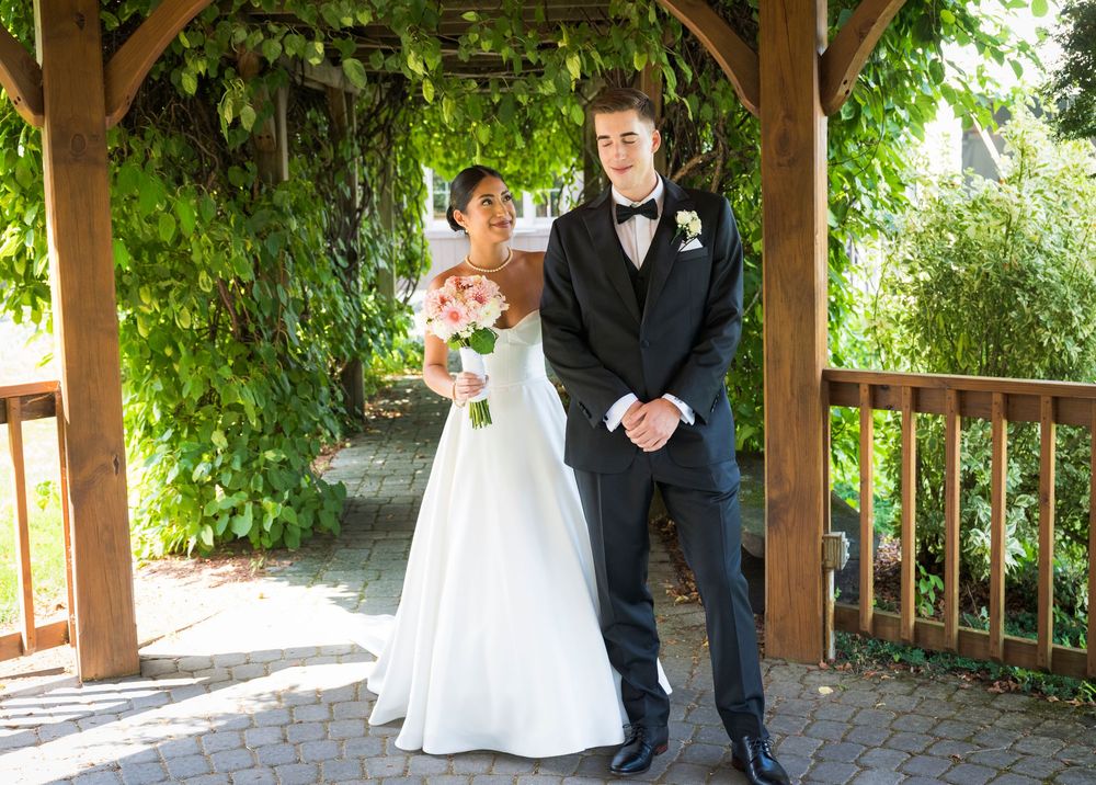 Newlyweds pose under a wooden pergola covered in lush green vines.