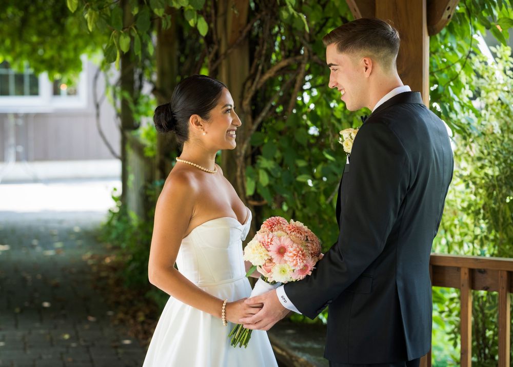 Wedding couple shares an intimate moment under lush green foliage during an outdoor summer photoshoot.