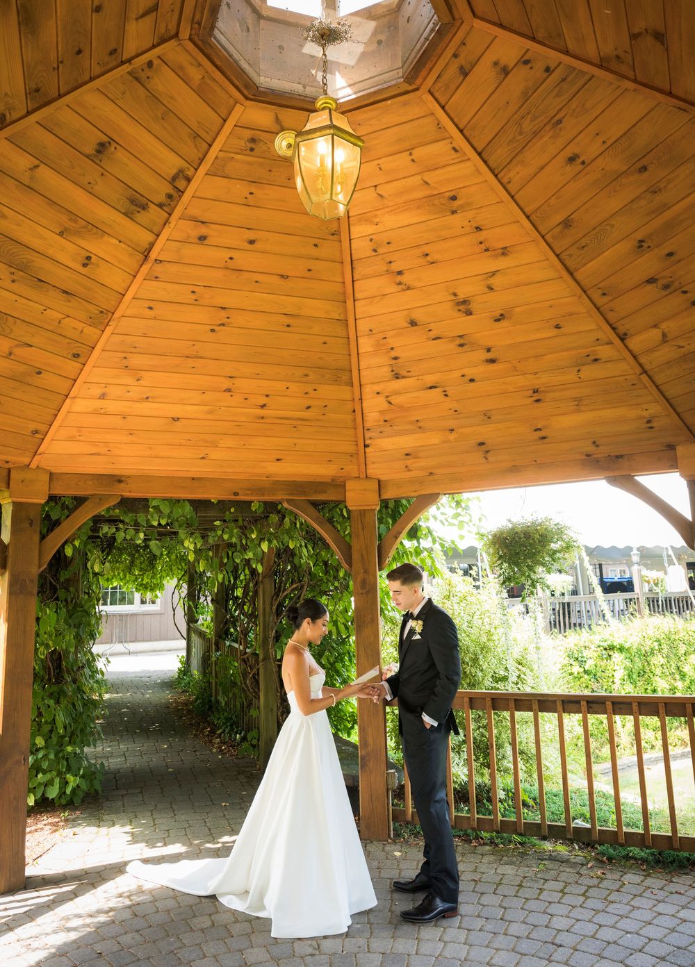 Bride and groom stand together under rustic wooden gazebo with vaulted ceiling.