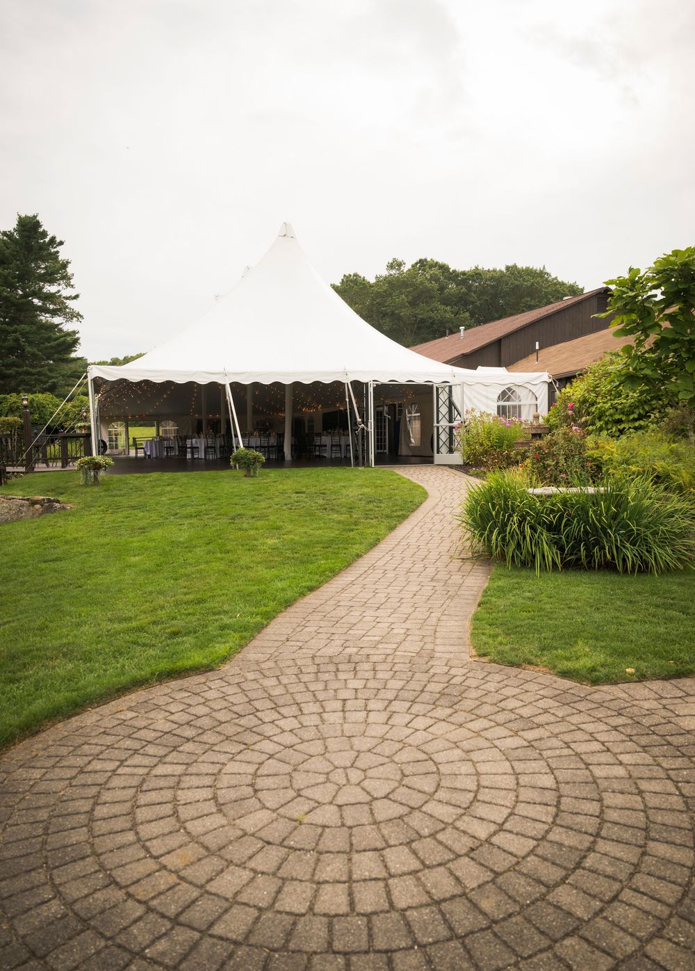 A series of curved stone pathways winding through a green lawn towards white tents and buildings in the distance.