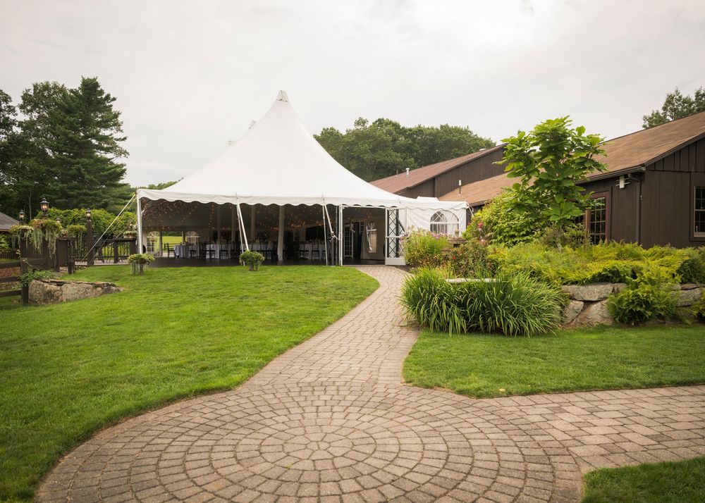 A curved brick paver pathway leads to an outdoor wedding venue with white tent in the distance.