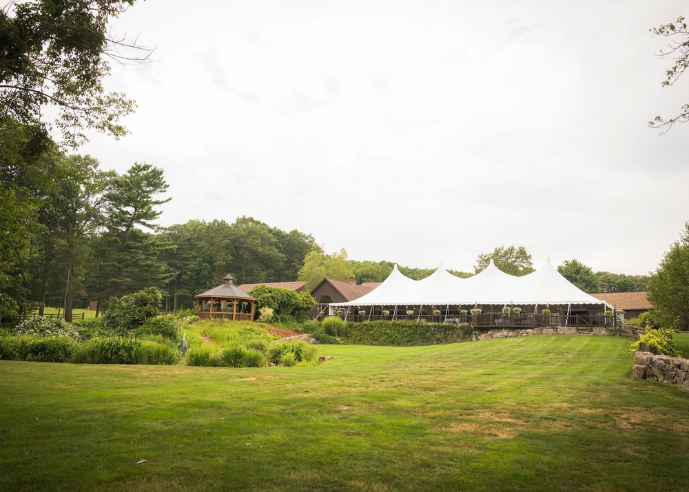 Panoramic view of a countryside wedding venue with white tents set up in a grassy field.