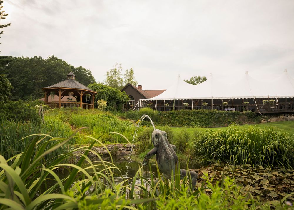 Scenic view of a rustic farm venue with lush greenery and a wooden gazebo in the distance.