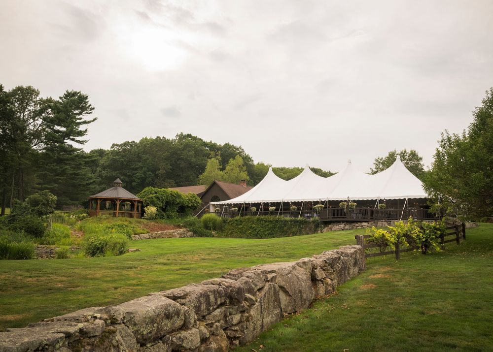 Panoramic view of wedding venue grounds with stone wall and reception tent in distance.