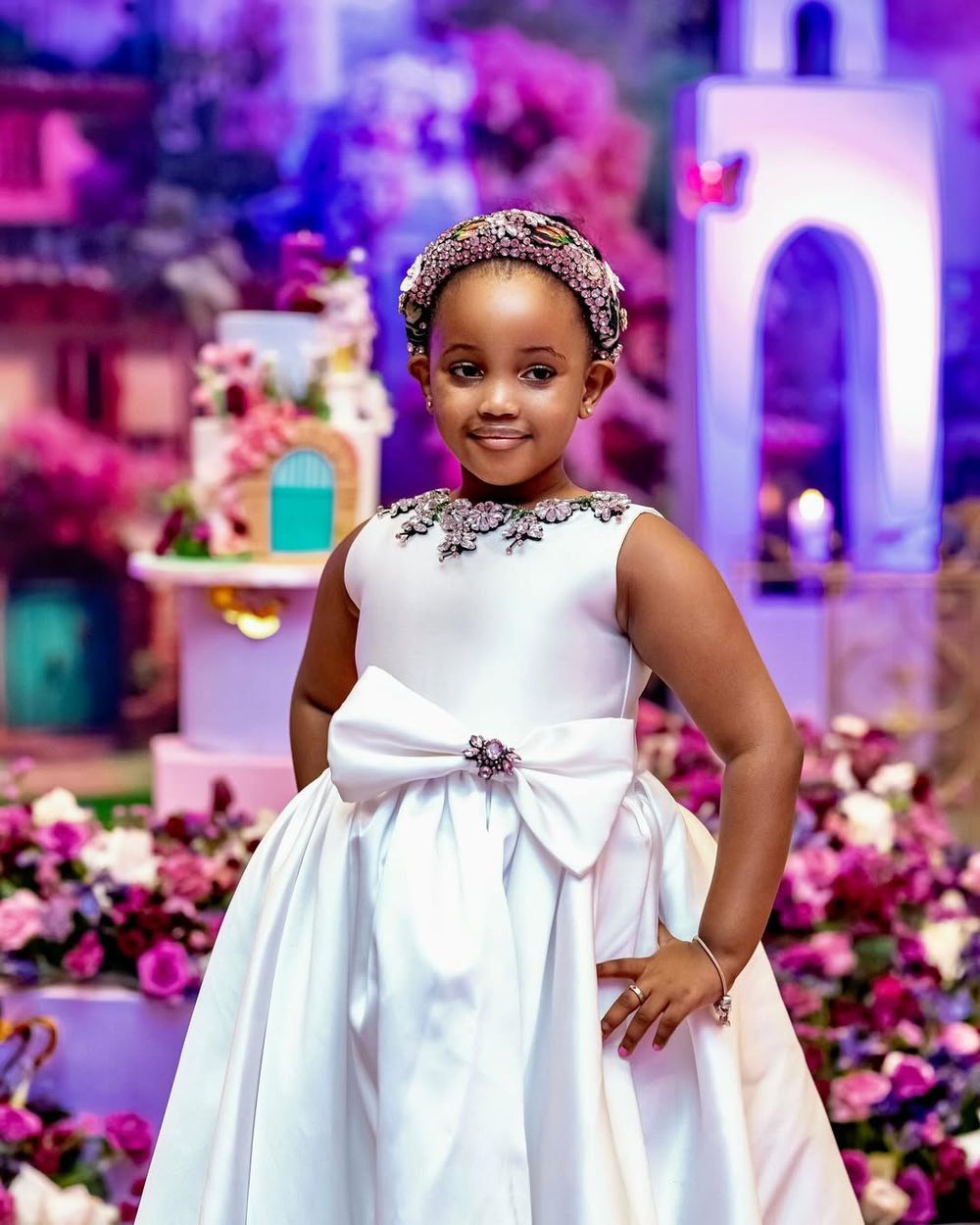 Beautiful white satin dress with bow detail and embellished neckline against purple and pink floral backdrop.