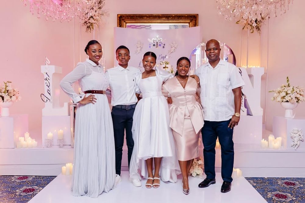 A group of people pose together in front of a decorated pink and white backdrop at a formal event.