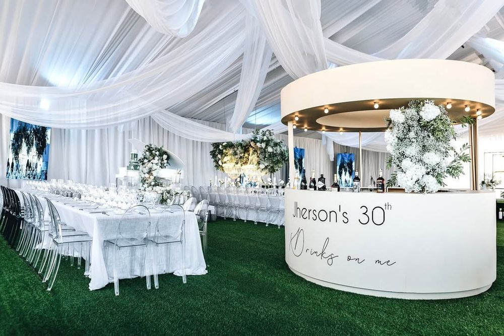 Modern white tent wedding reception setup with elegant decor, round tables and a custom circular bar.