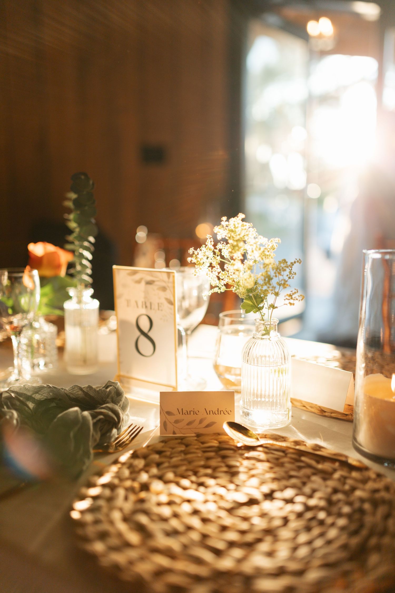Wedding reception table setting with table number 8, candles, and small floral arrangements in warm light.