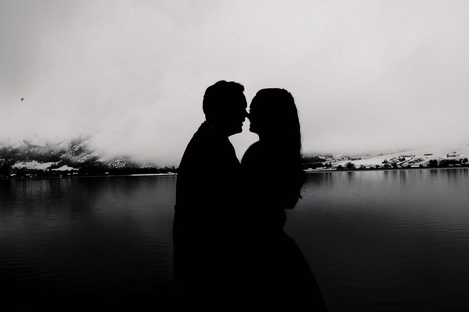 Romantic silhouette of a couple against a serene waterfront landscape in black and white.
