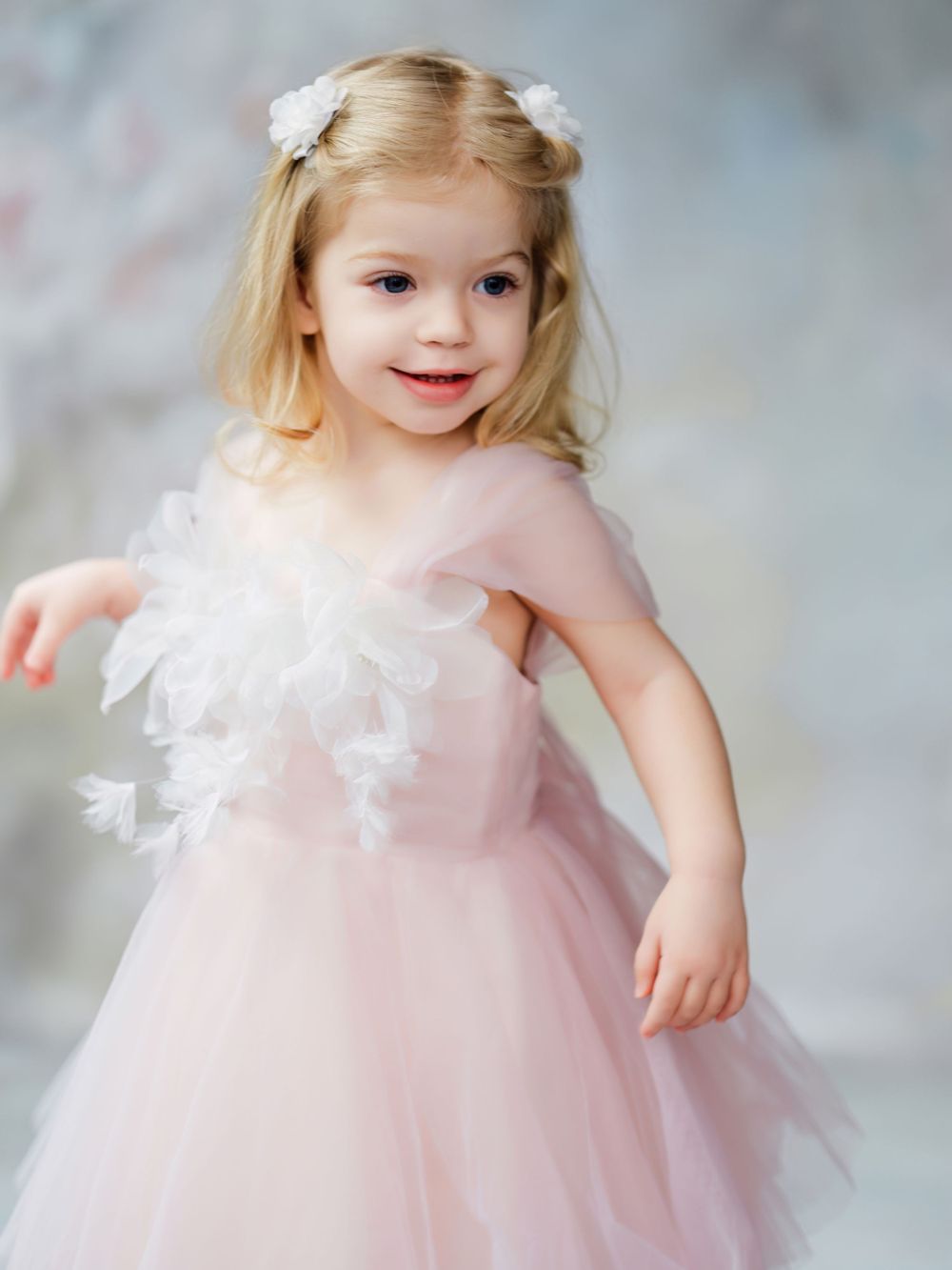 Young child in pink tulle dress with white floral accents poses against soft grey background in Bellevue studio.