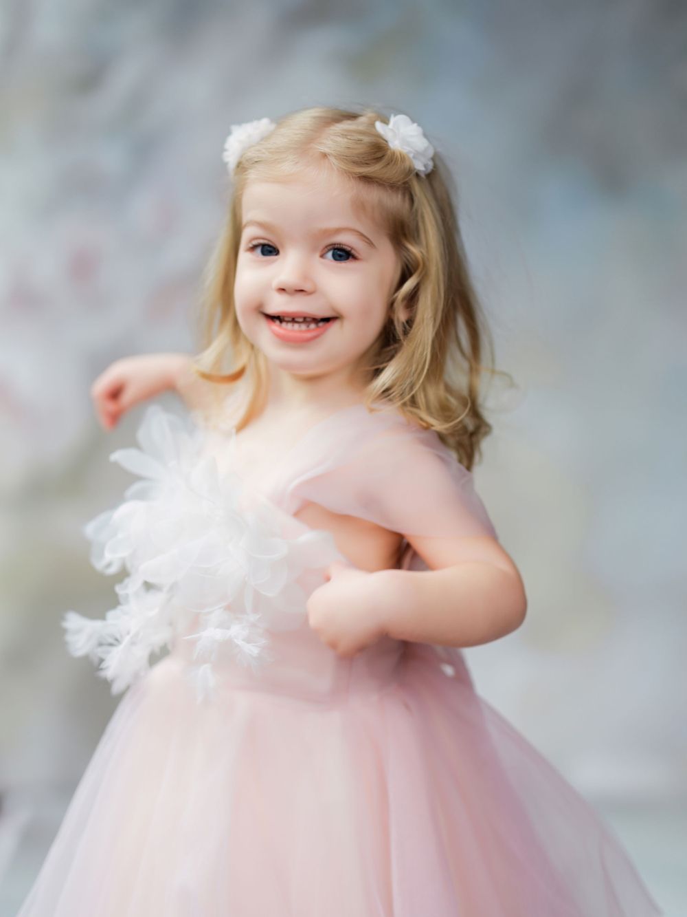 A child in a pink tulle dress with feather accents poses for a portrait against a soft blurred background in Bellevue studio.