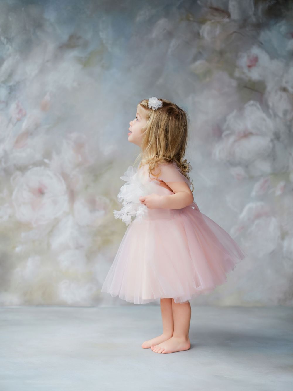 Young child in pink tulle dress poses dreamily against cloudy backdrop in Bellevue studio.