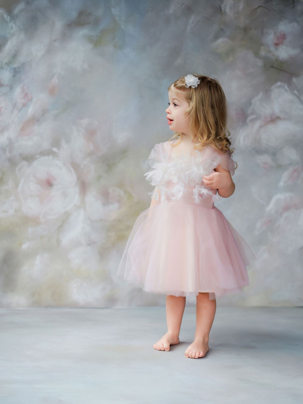 A young girl in a pink tulle dress stands barefoot against a dreamy grey backdrop with soft lighting in Bellevue studio.