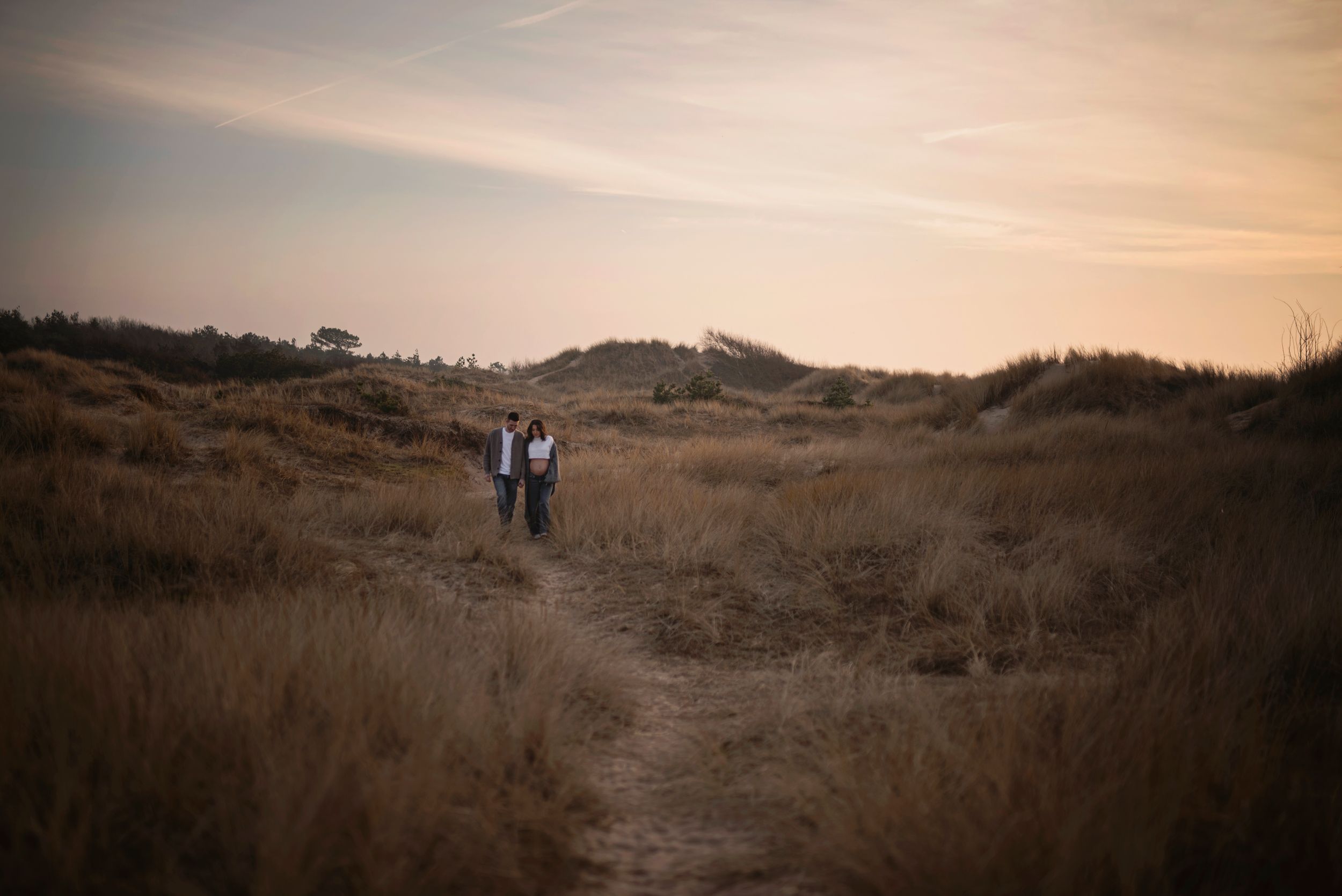 Two people standing on hilltop path at dusk with golden sky.