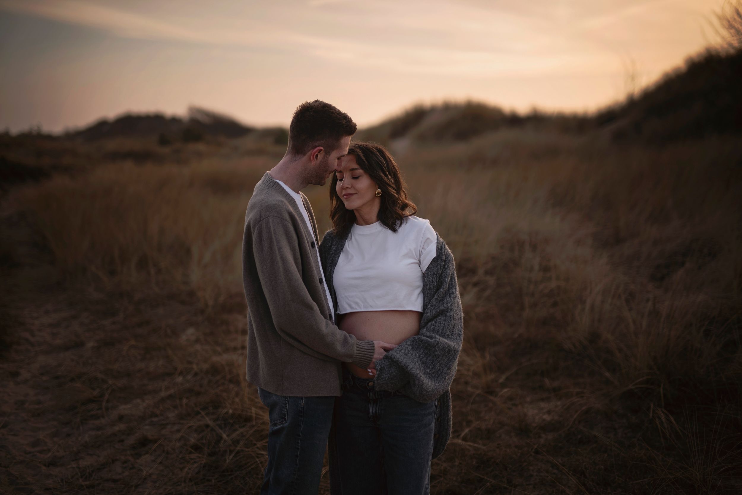 Two figures embrace in warm sunset light on a grassy hillside landscape during golden hour.
