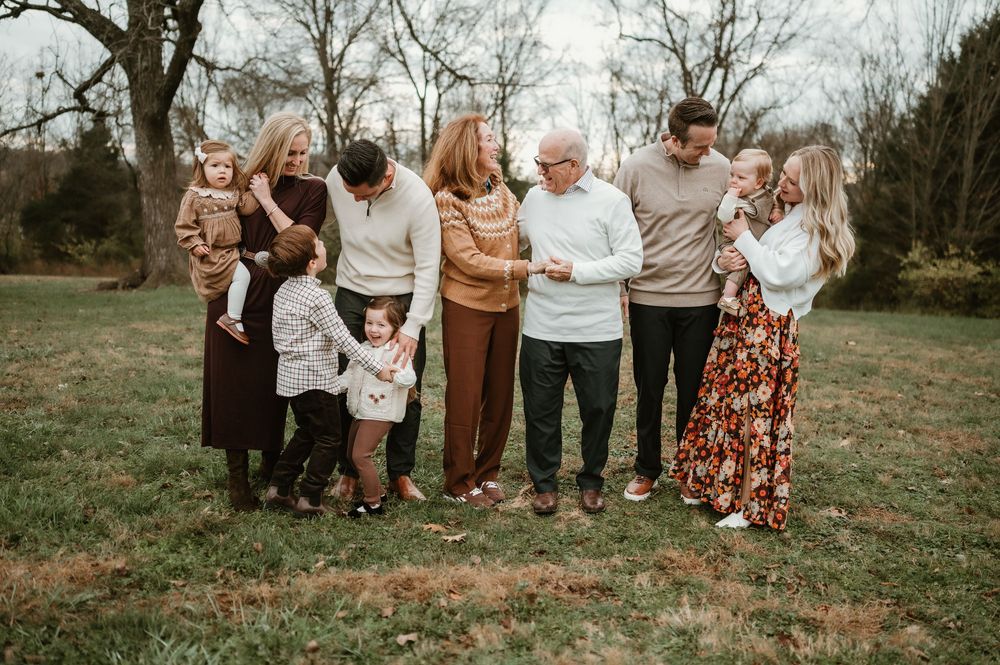 Multi-generational family gathering outdoors in autumn, sharing a joyful moment on a green lawn surrounded by trees.