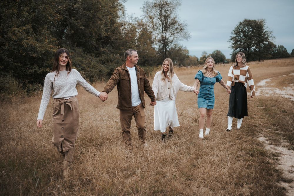 A joyful group walks hand in hand through a golden autumn field on a winding dirt path.