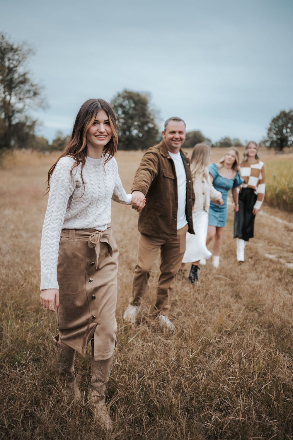 People hold hands while walking in line through a golden autumn field on an overcast day.