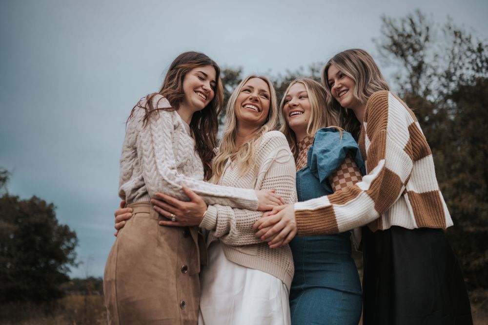 Four friends sharing a laugh together while hugging outdoors in casual fall attire.