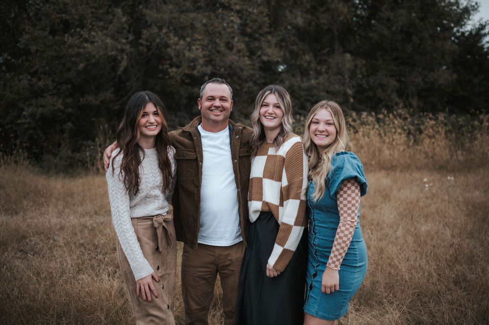 A group poses together outdoors in casual fall attire against a backdrop of dry grass and trees.