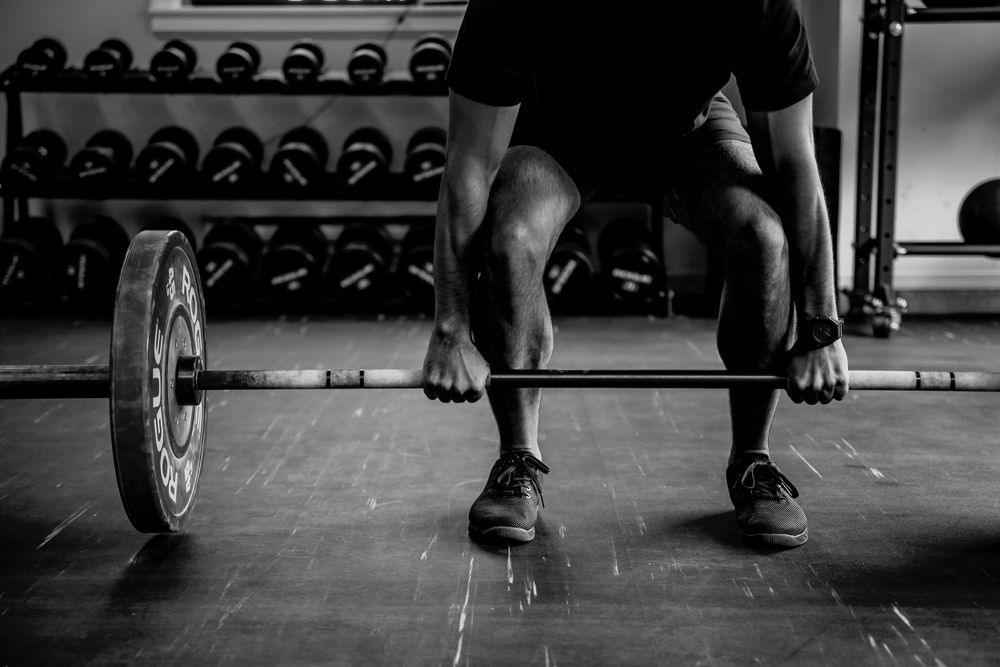 Close-up shot of weightlifter's legs preparing to lift barbell in dark gym setting.