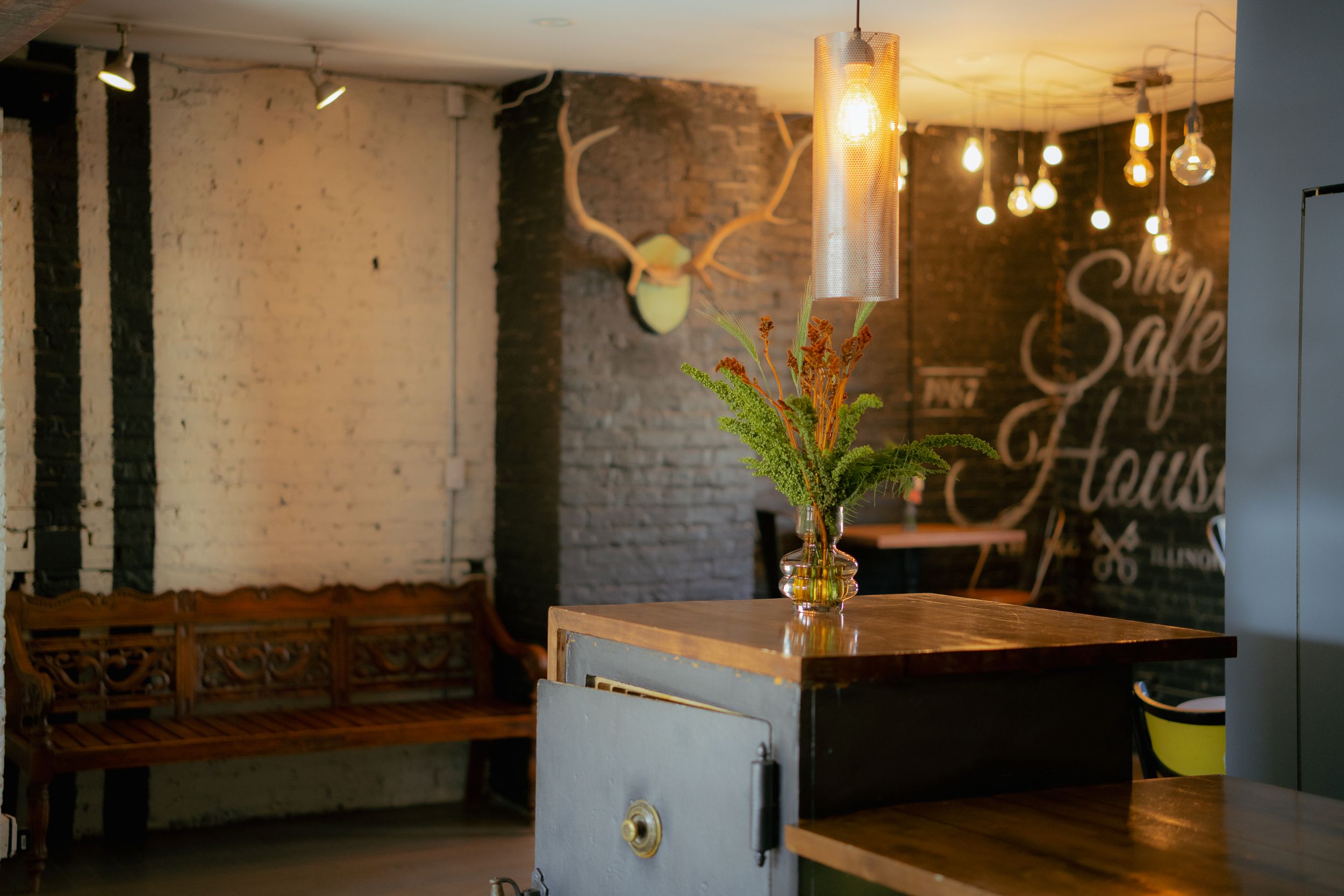 Rustic interior of a cafe with wooden bench seating, brick wall, antler decor and warm pendant lighting.