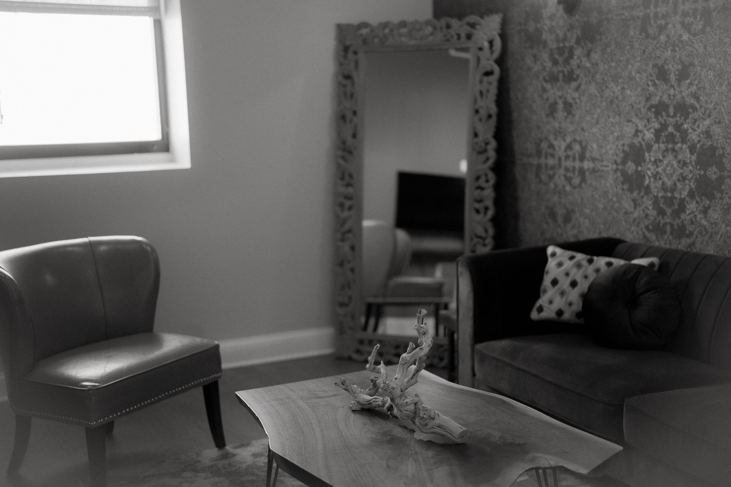 Modern living room features a gray accent chair, decorative mirror, and coffee table in black and white tones.