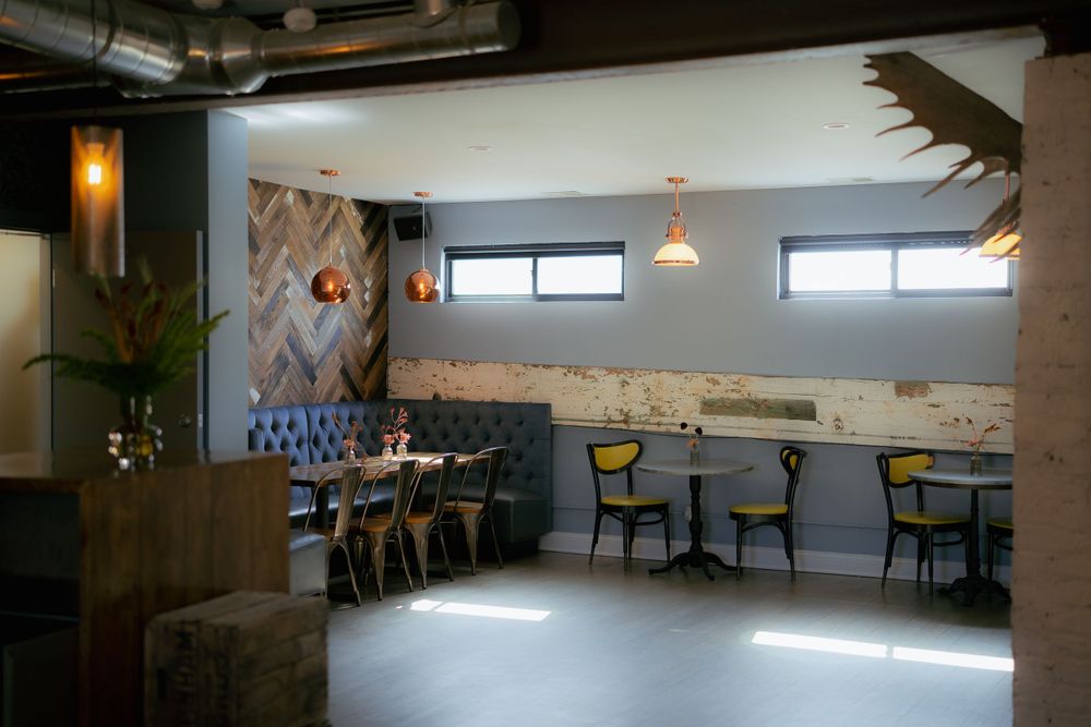 Modern restaurant interior with geometric wall design, banquette seating, and natural light streaming through high windows.