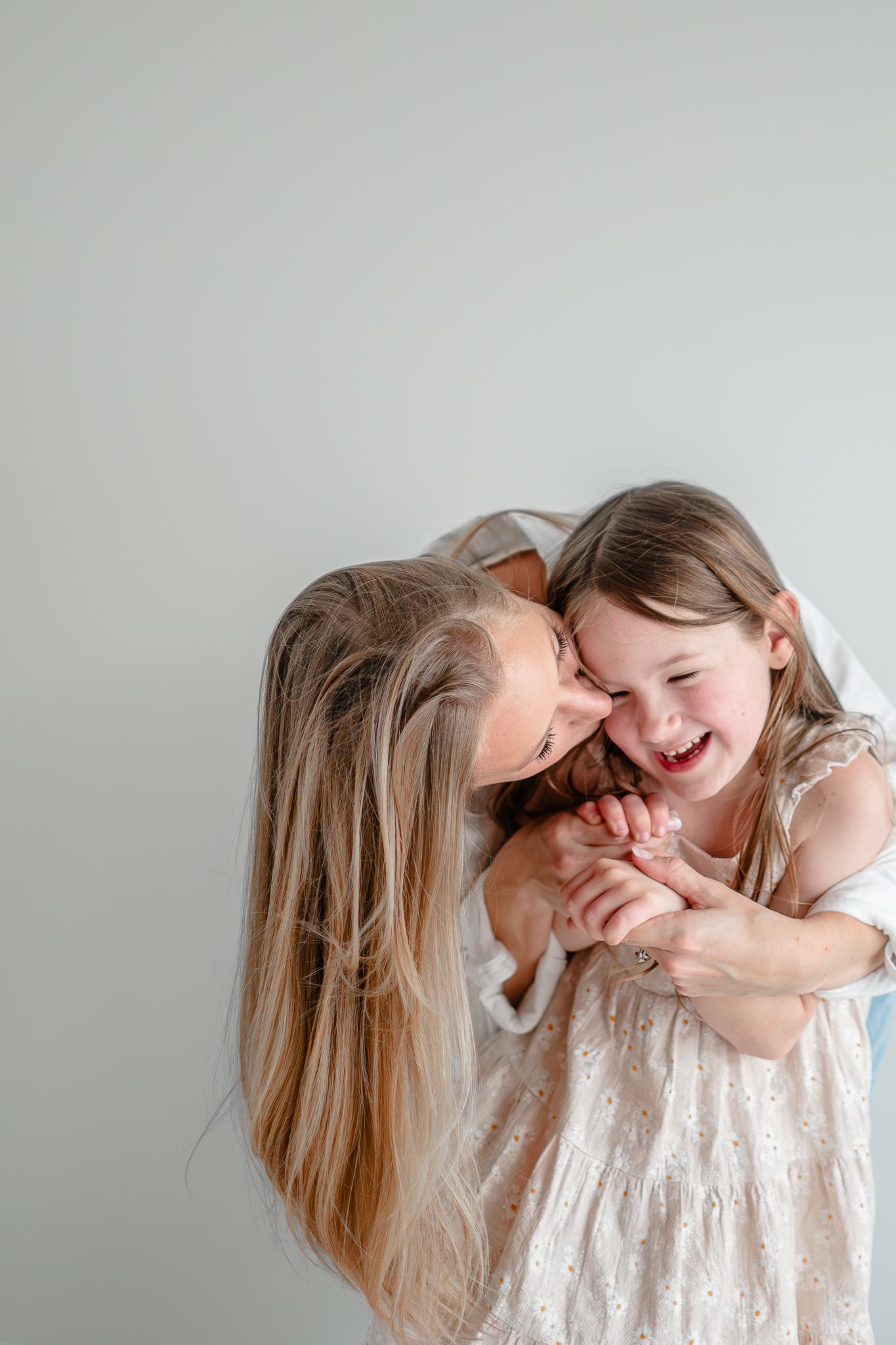 A tender moment of affection and laughter between two people wearing white, captured against a light gray background.