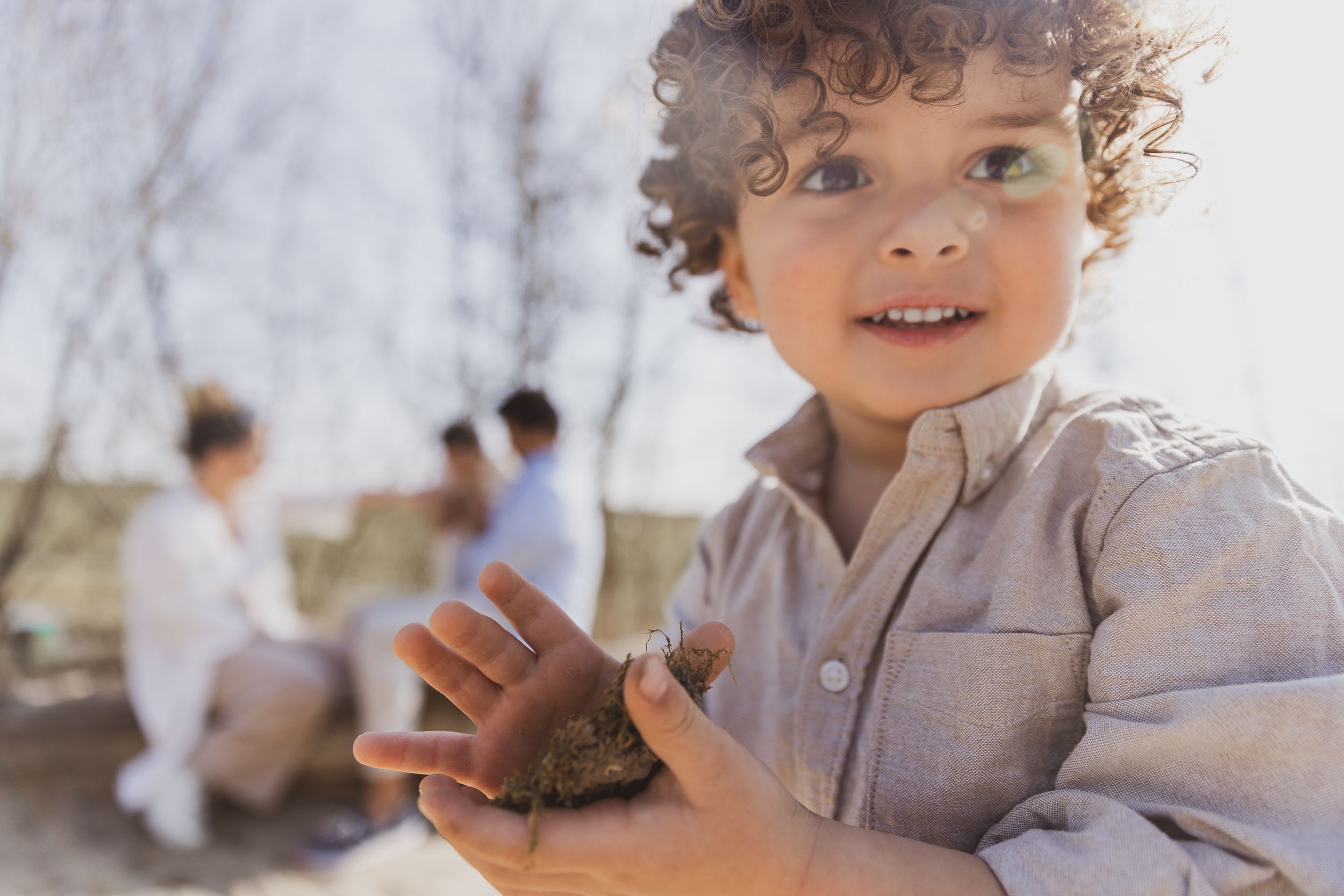Child with curly hair smiles while playing outdoors. Gezinsfotos net even anders.