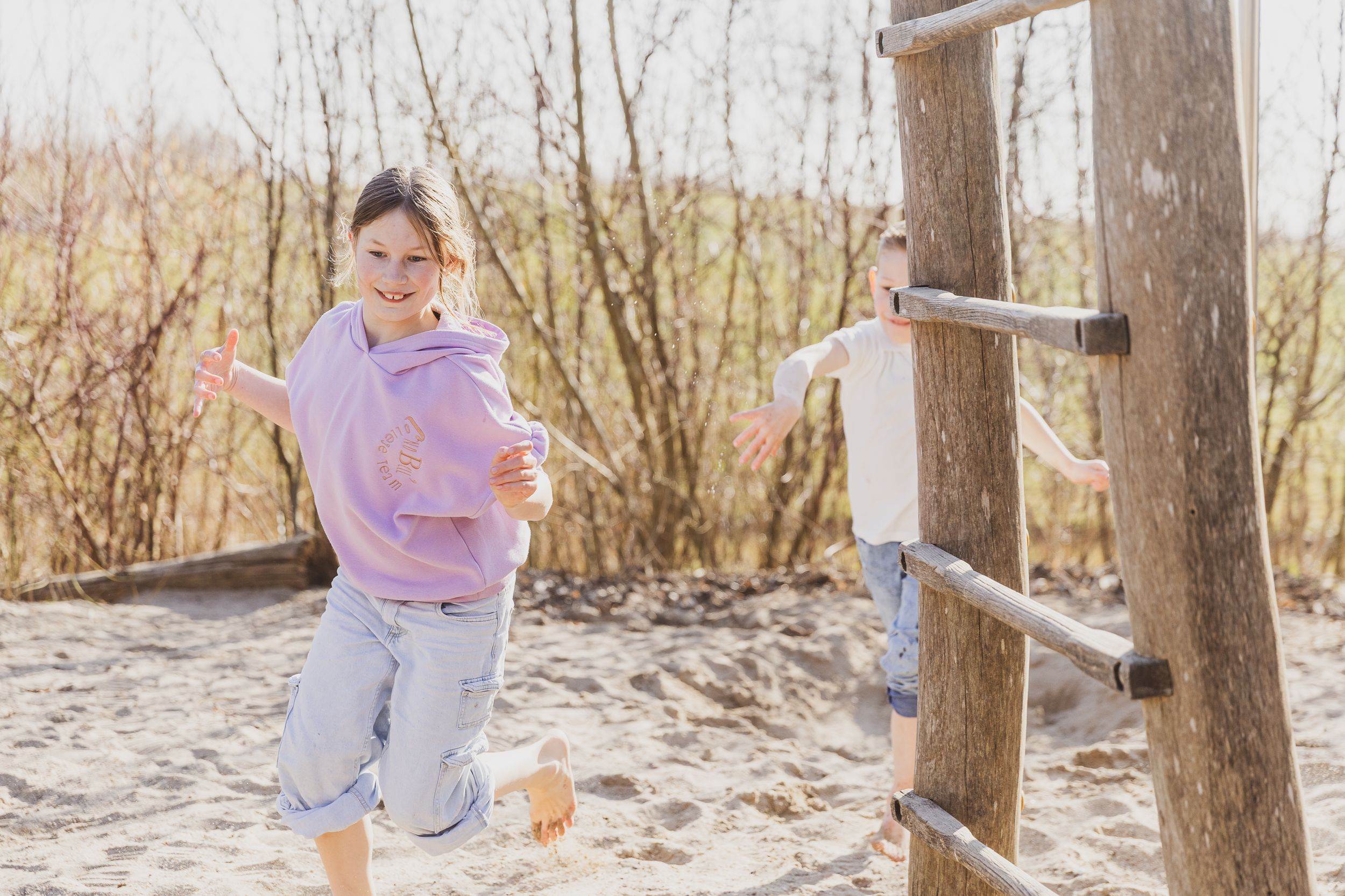 Child playing on a sandy playground near wooden climbing structure. Op de foto als jezelf.