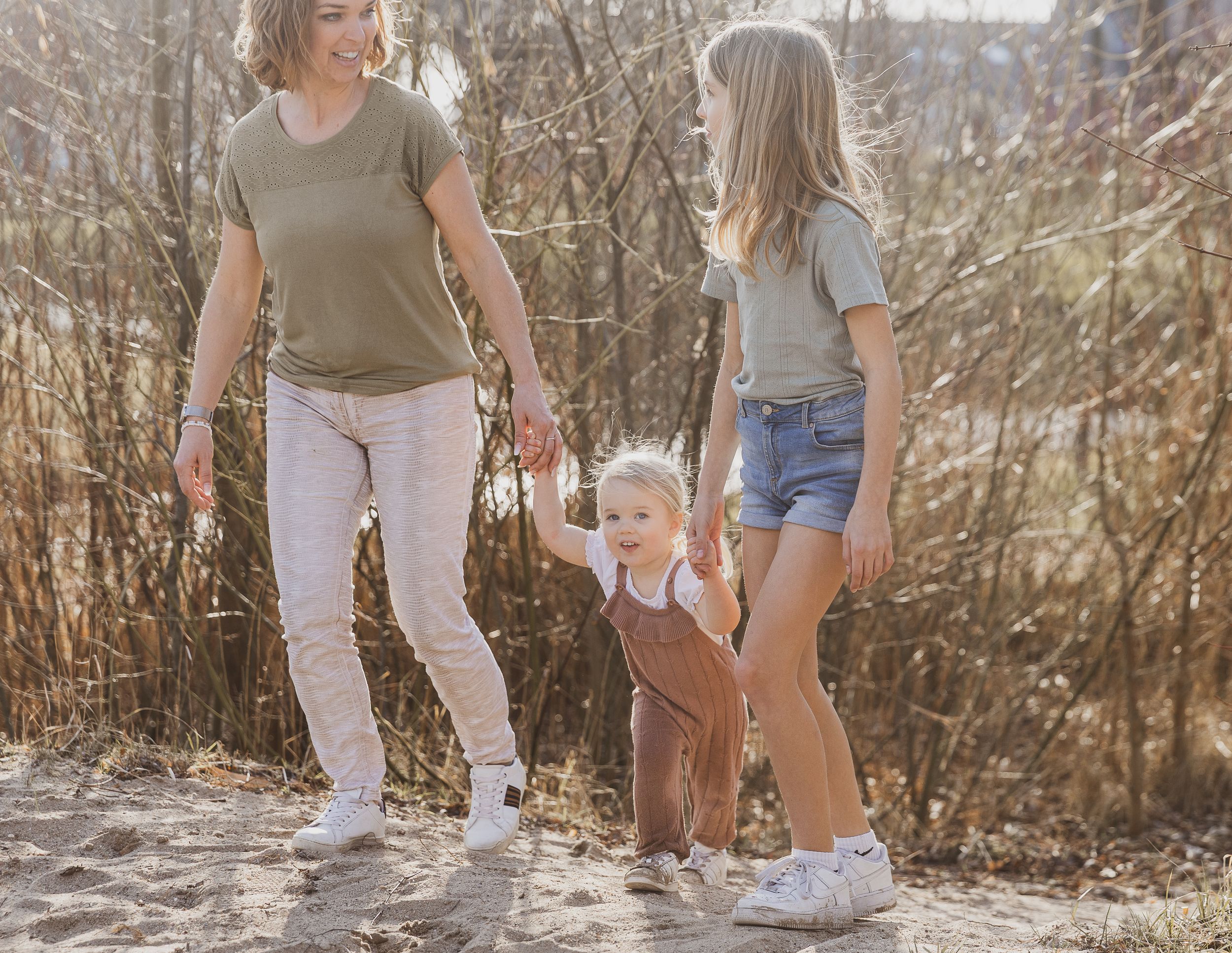 Family members walk together on a sandy path surrounded by autumn brush and trees. Pure fotografie.