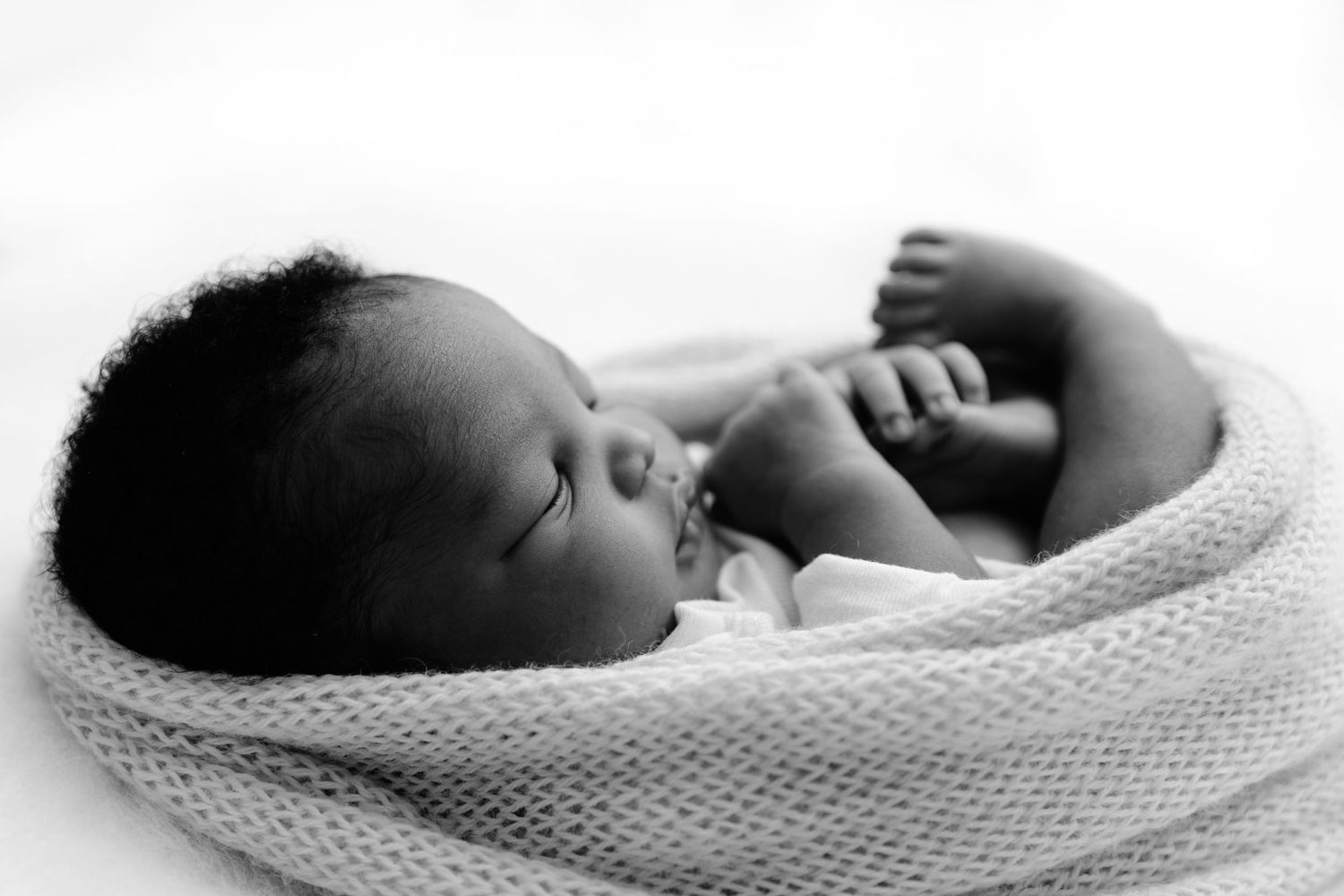 A peaceful sleeping newborn baby wrapped in a soft white knit blanket, captured in black and white photography.