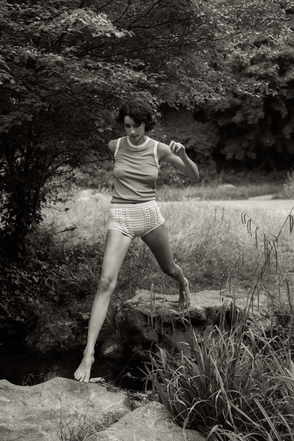 A series of black and white photos showing legs and feet dancing or moving through tall grass in a natural setting.