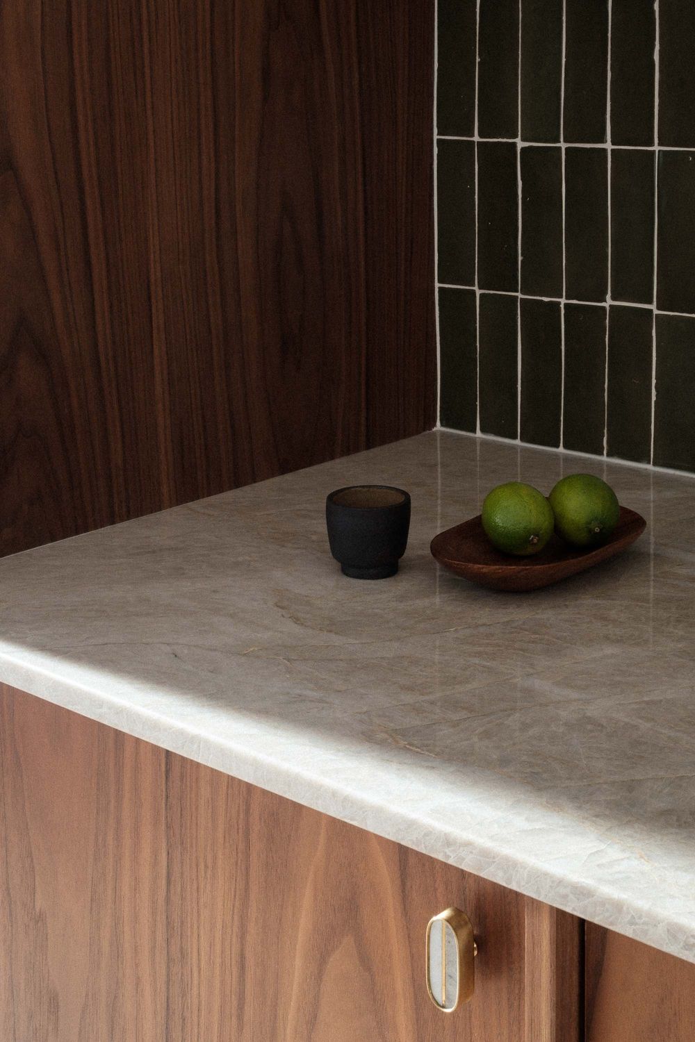 Modern kitchen cabinet corner with white marble countertop and dark wood paneling against a white tiled wall.